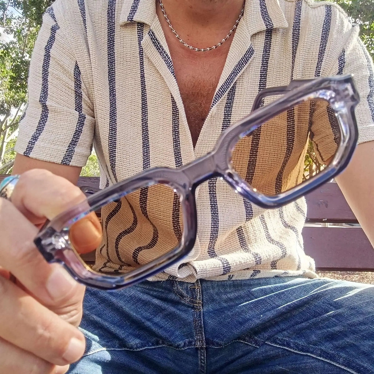 Gafas de sol con montura azul translúcida de diseño geométrico y cristales marrones sostenidas por una mano.