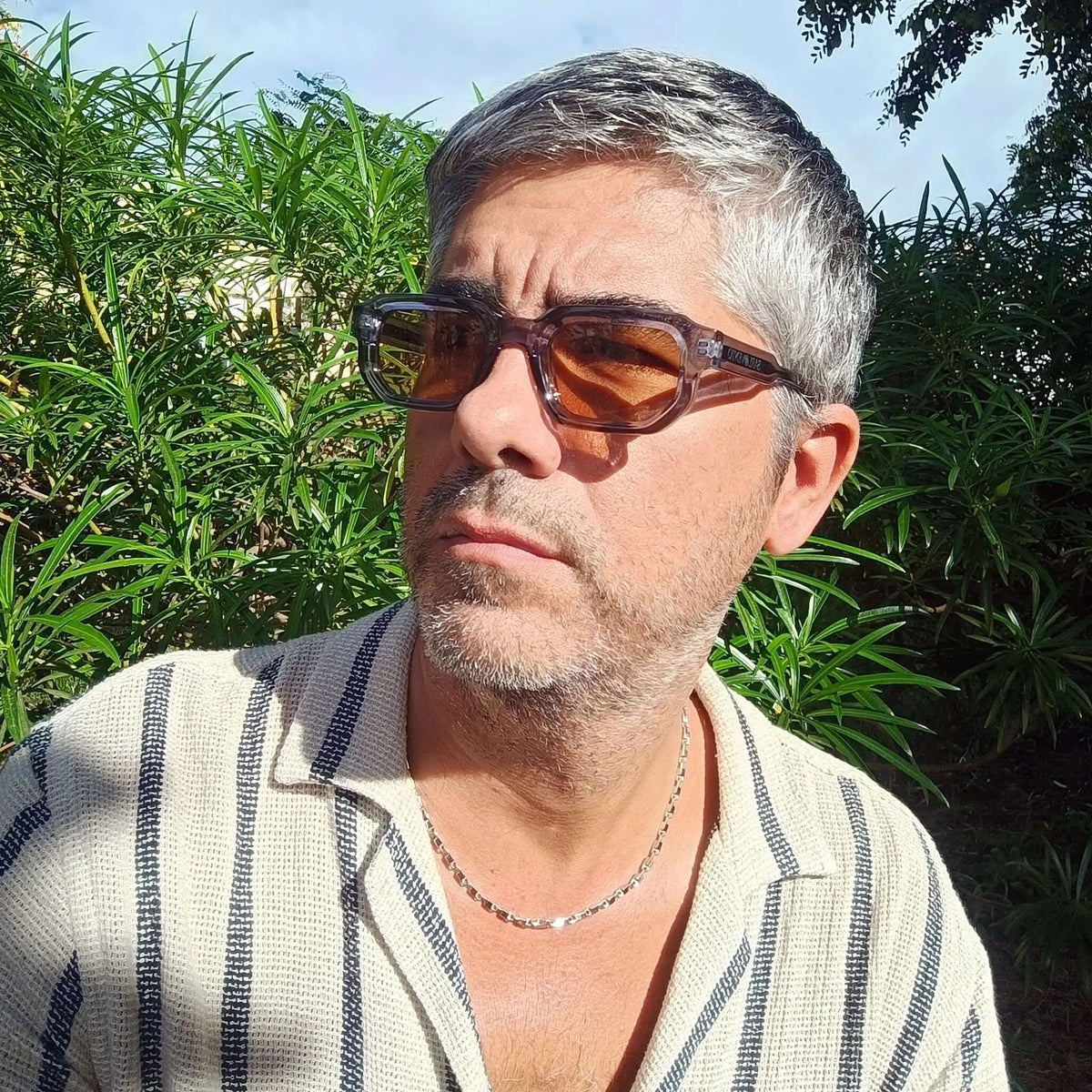 Hombre con gafas de sol de montura azul traslúcida rectangular y lentes marrones al aire libre.