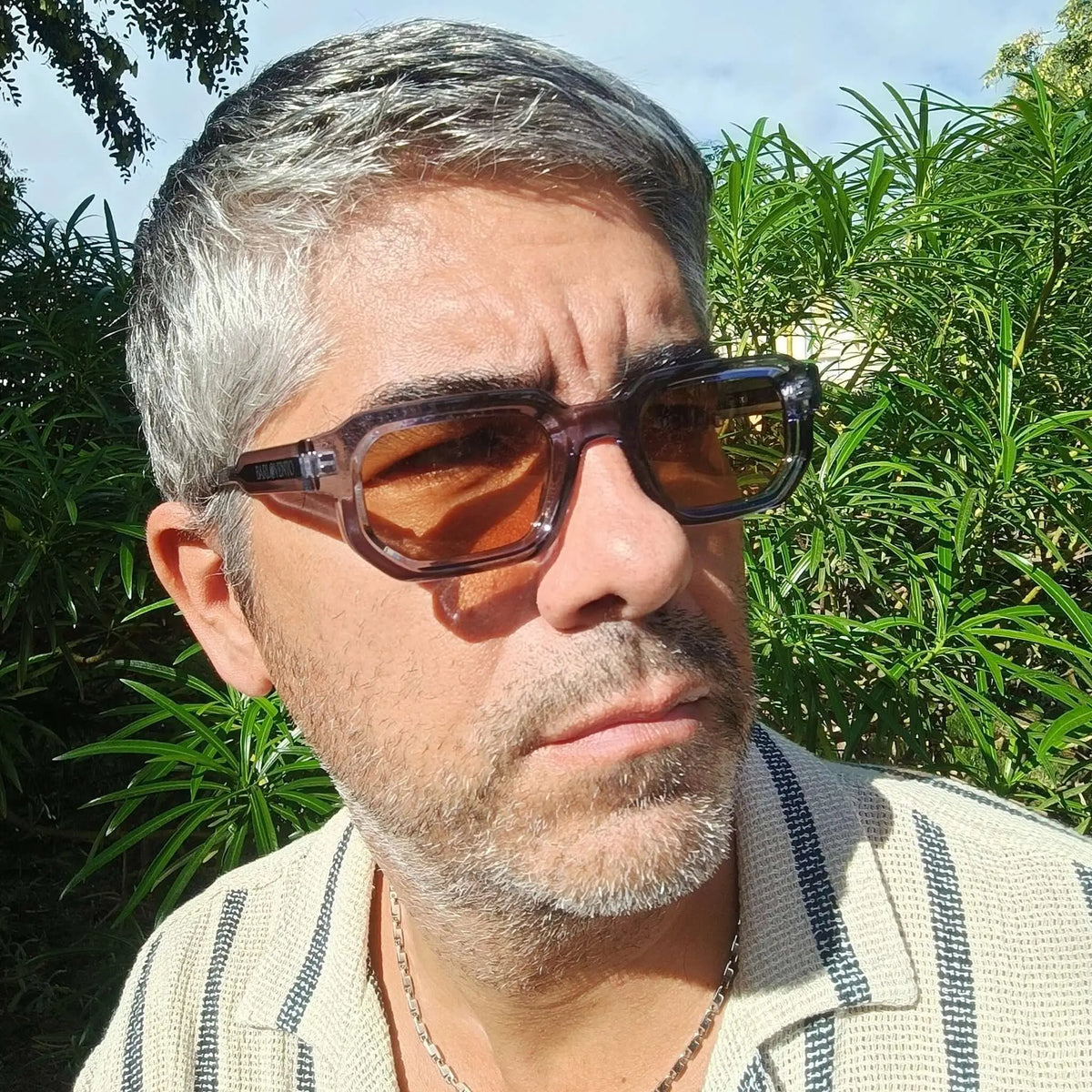 Gafas de sol de montura gruesa azul traslúcido y lentes marrones de estilo rectangular en un hombre al aire libre.