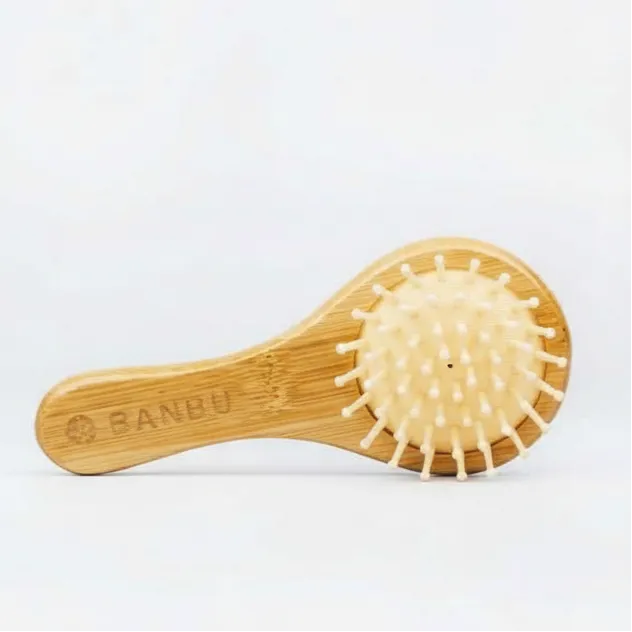 Cepillo de viaje Banbu de madera clara con púas redondeadas sobre base neumática beige, sobre fondo blanco neutro.