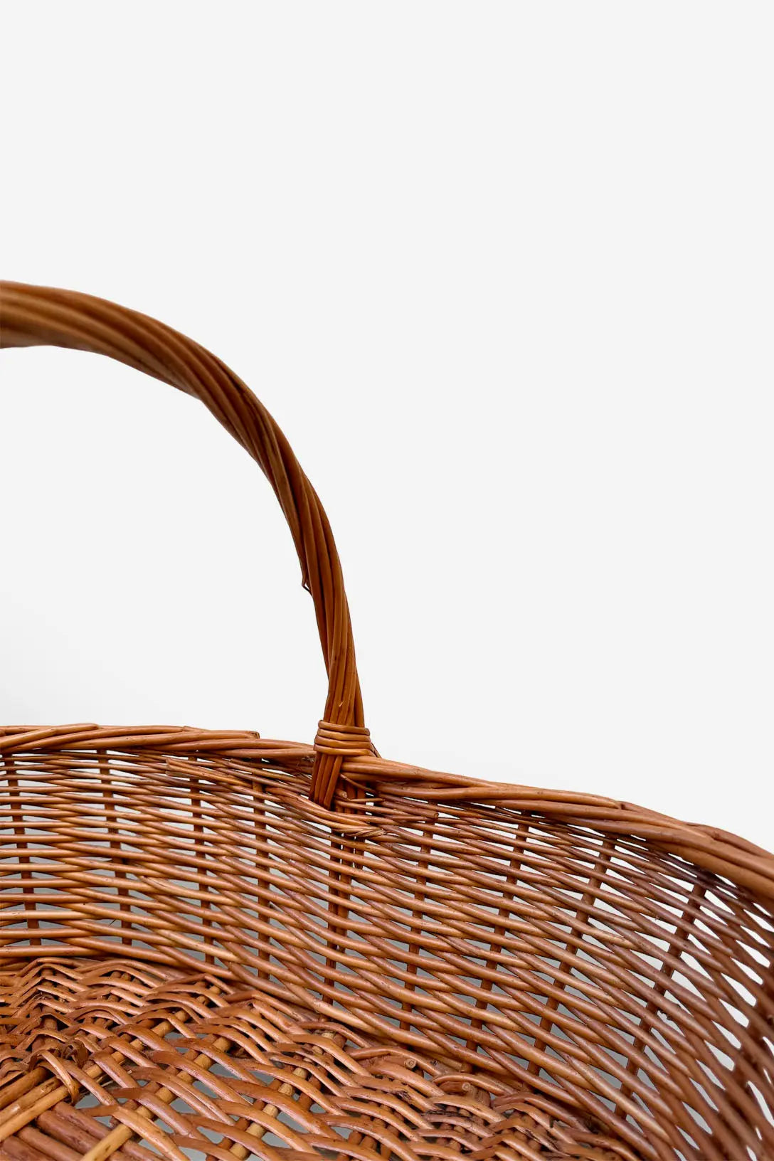 Cesta ovalada de mimbre natural trenzado en tono marrón con asa arqueada, estilo artesanal rústico sobre fondo blanco.