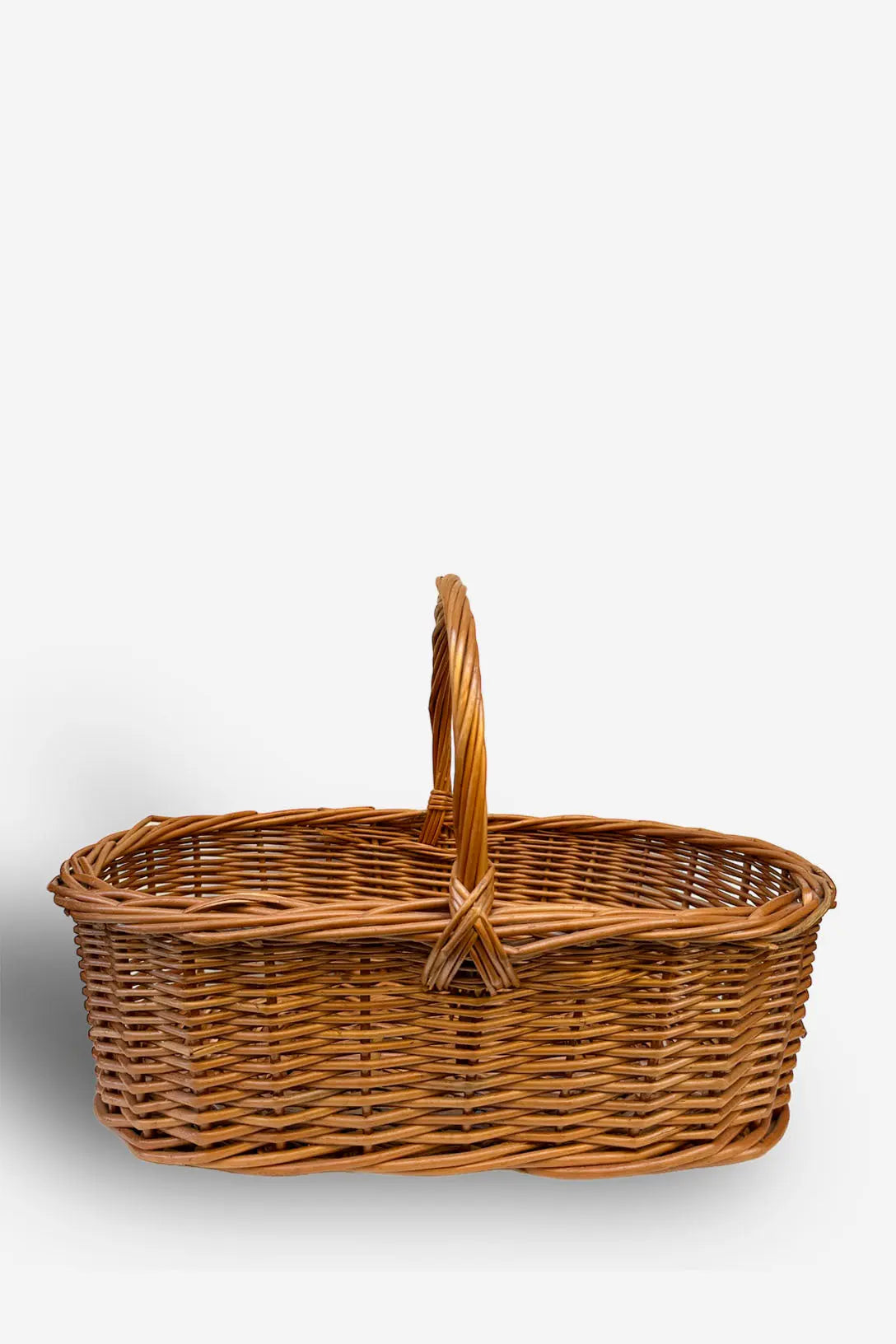 Cesta ovalada de mimbre natural con trenzado artesanal y asa central, diseño rústico en color marrón claro.