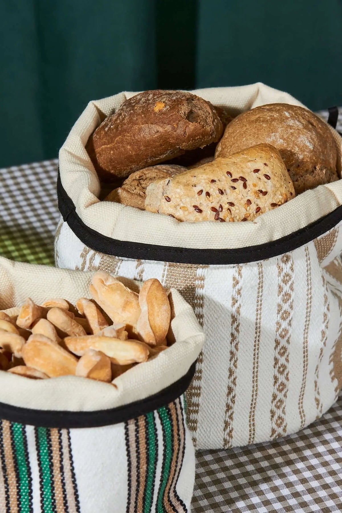 Dos cestos de tela con rayas verdes y beige, rellenos de panes y picos, sobre un mantel a cuadros.