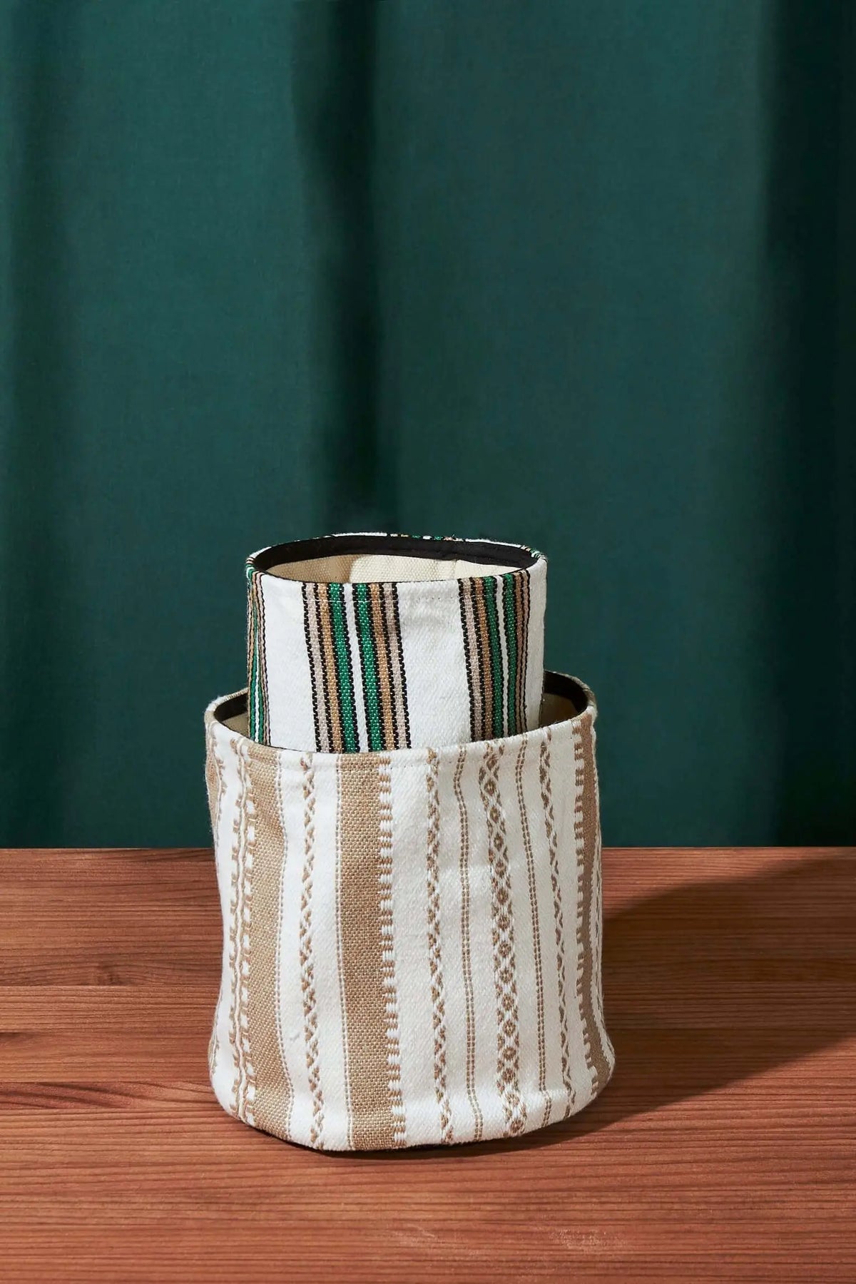 Cestos cilíndricos de tejido artesanal en tonos beige y verde con patrones de rayas verticales sobre fondo de madera.