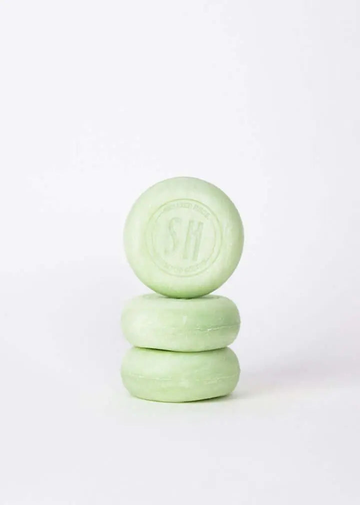 Pila de tres pastillas de champú sólido redondas de color verde claro sobre un fondo blanco minimalista.