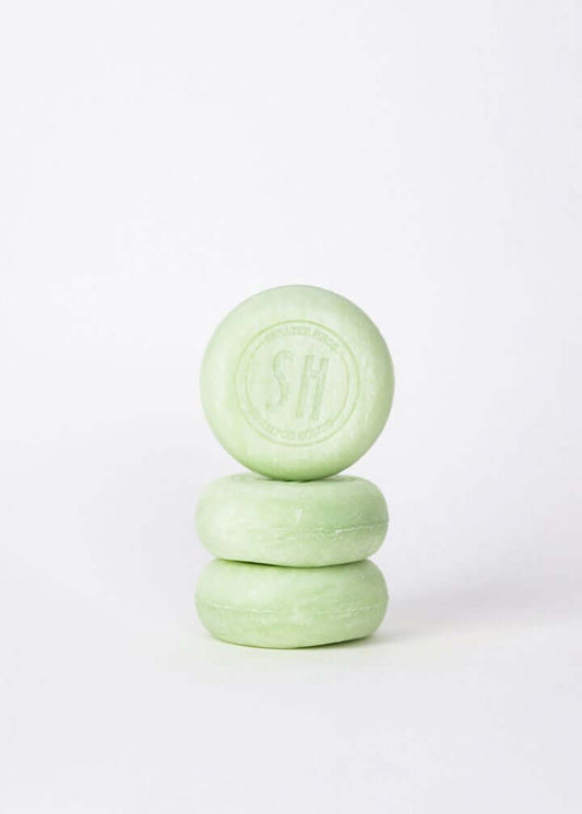 Pila de tres pastillas de champú sólido redondas de color verde claro sobre un fondo blanco minimalista.