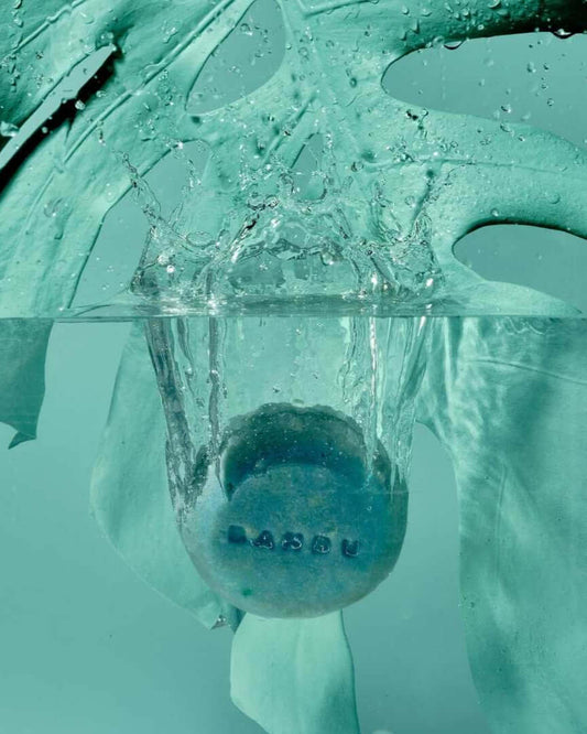 Champú Sólido ECO Cabello Rizado Método Curly FLUFFY sumergido en agua con hojas verdes, destacando su textura y frescura.