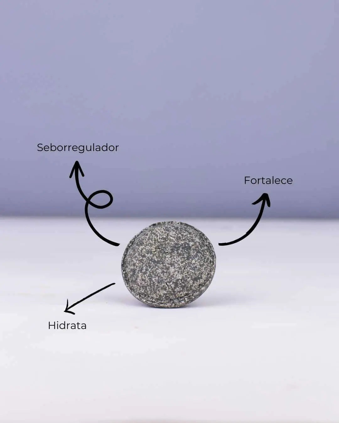 Champú sólido gris oscuro Mare de Banbu sobre fondo claro, con flechas indicando sus beneficios: regula, hidrata y fortalece.