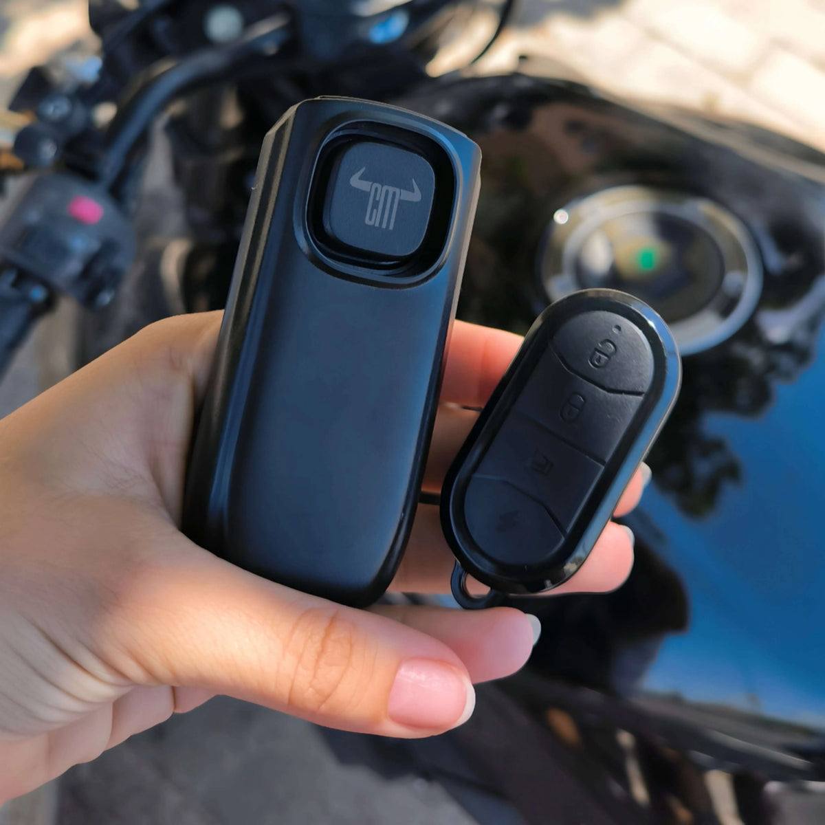 Alarma inalámbrica negra ChuchesMoto con mando y dispositivo principal mate sostenidos sobre una motocicleta.