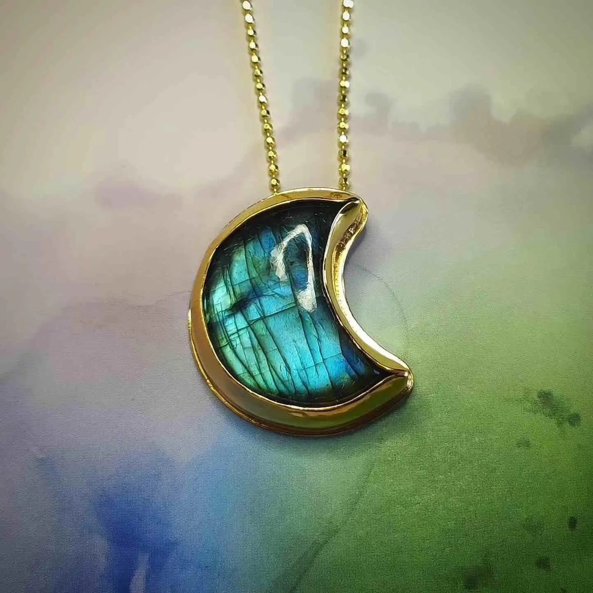 Colgante en forma de media luna de labradorita azul con marco dorado, diseño elegante y moderno.