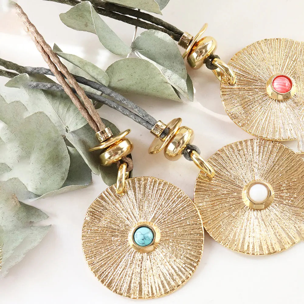 Collares de estilo bohemio con medallas doradas y piedras turquesas, rojas y blancas, sobre cuerdas en tonos naturales.