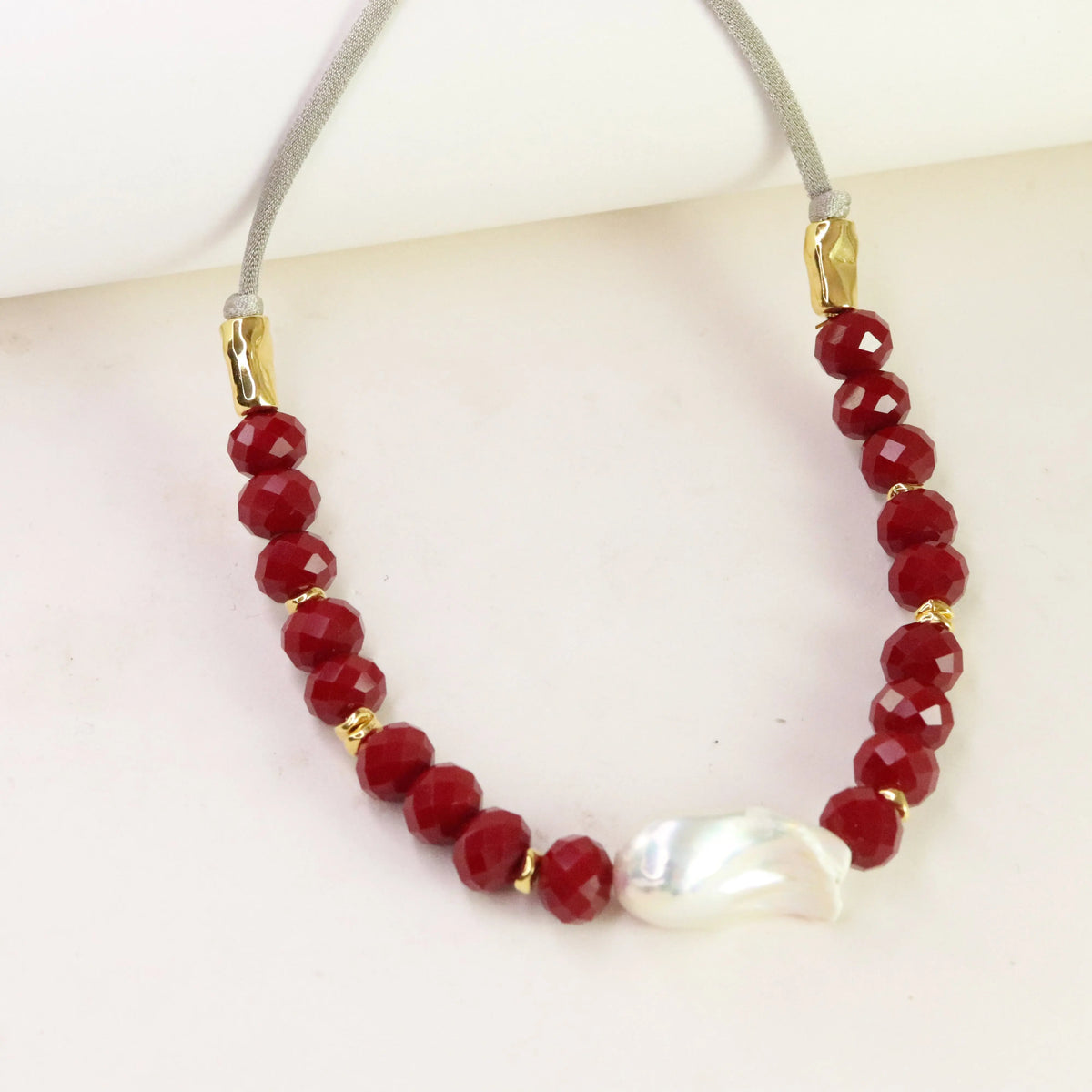 Collar de cuentas rojas facetadas y perla, con cadena gris y detalles en dorado. Estilo elegante y moderno.