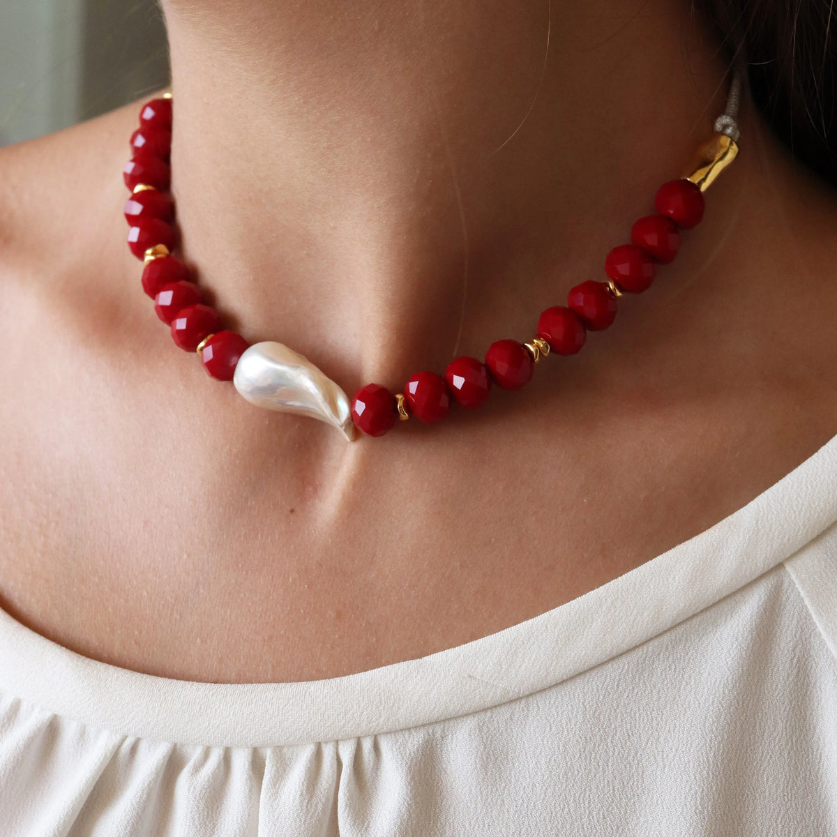 Collar de perlas rojas y doradas, con una perla blanca irregular en el centro, estilo elegante y moderno.