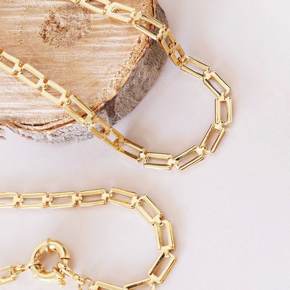 Collar de eslabones dorados, diseño moderno de acero inoxidable, sobre fondo de madera clara.