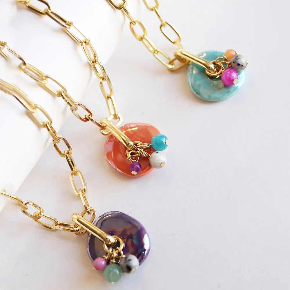 Collares de eslabones dorados con colgantes de cerámica en tonos coral, azul y púrpura, decorados con cuentas de colores.