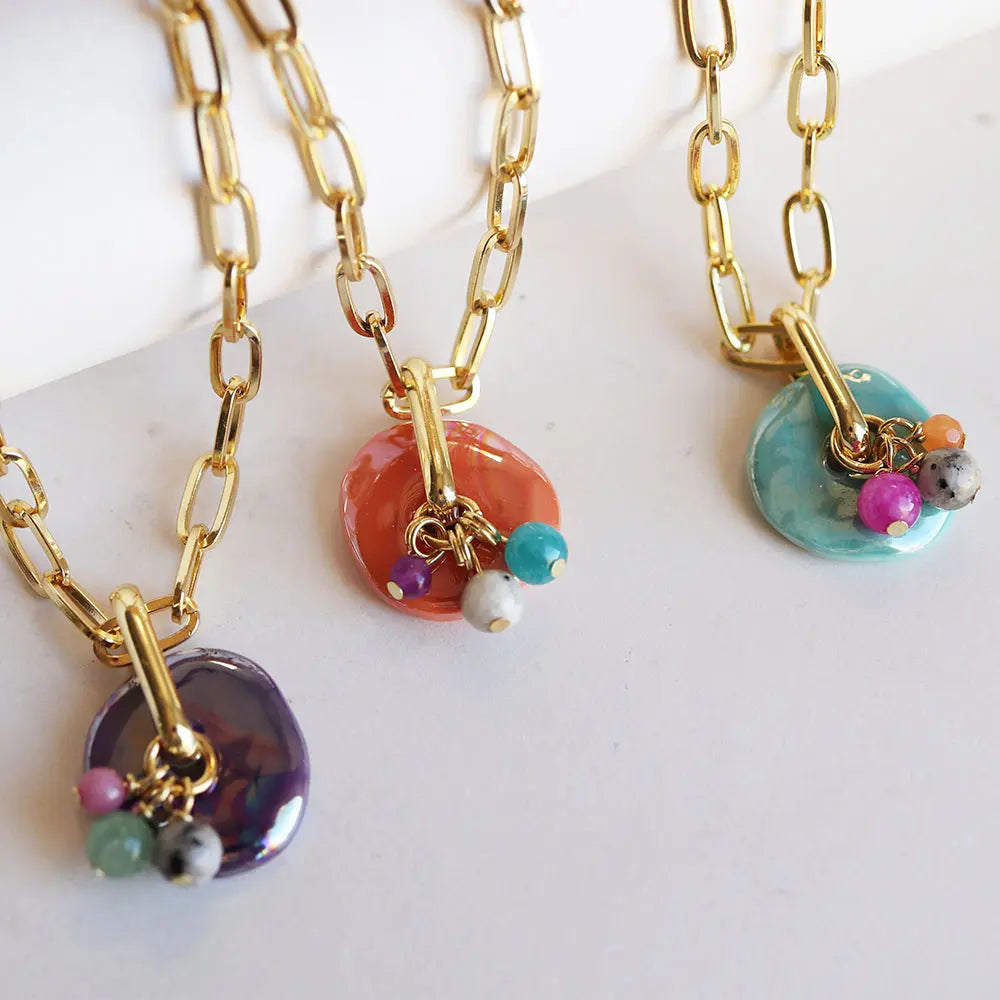 Collares de cadena dorada con colgantes de cerámica en tonos púrpura, naranja y azul, decorados con piedras de colores.