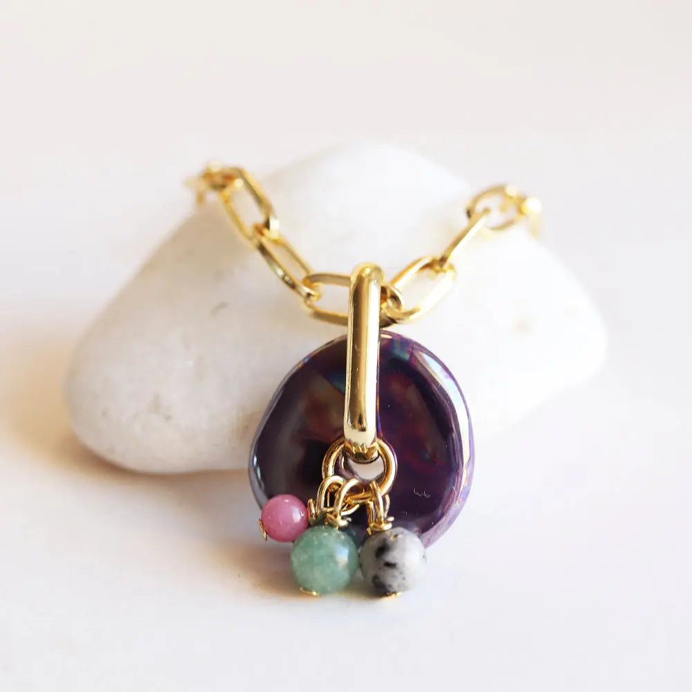 Collar de eslabones dorados con colgante de ópalo morado y piedras naturales en rosa, verde y gris.