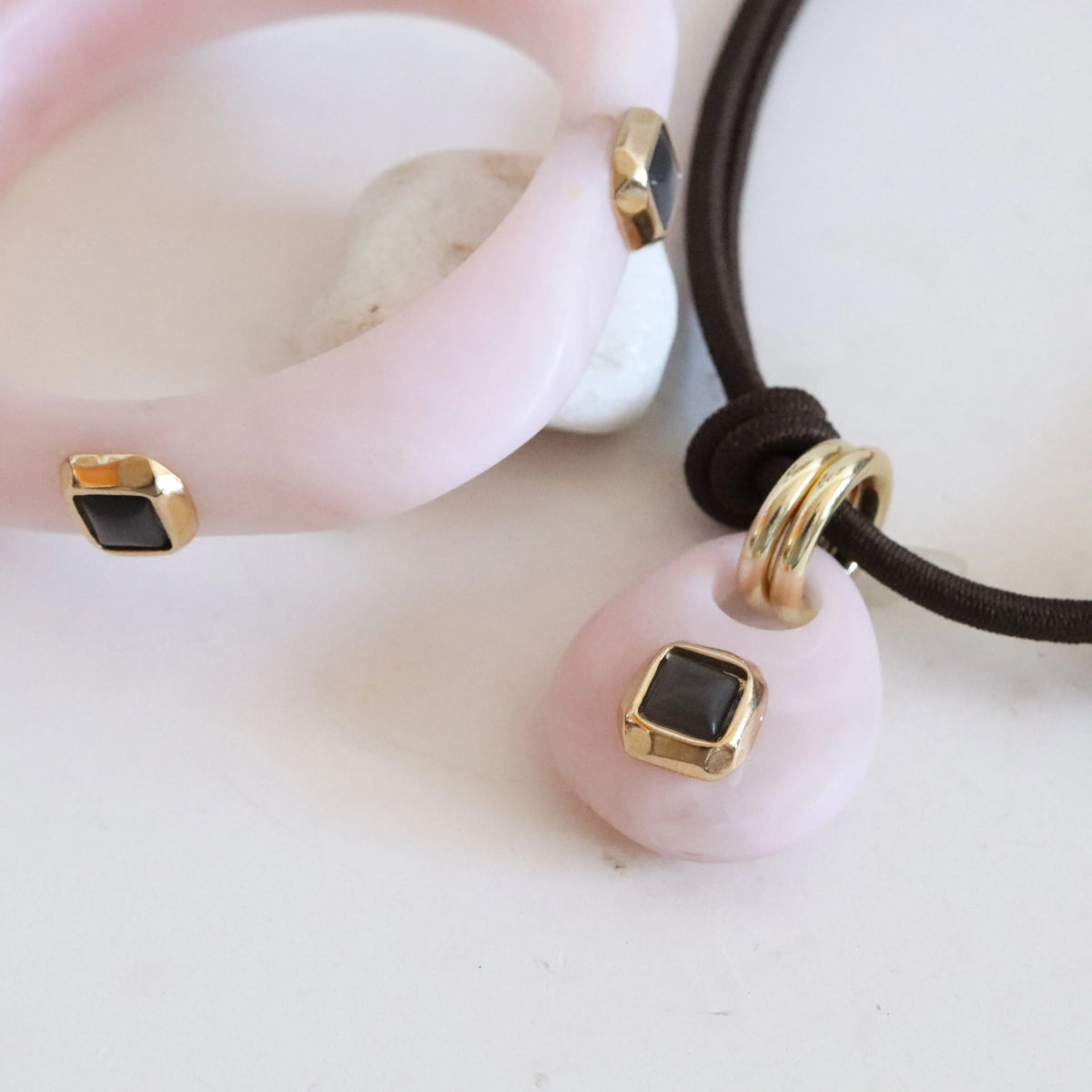 Collar y pulsera de acetato rosa con detalles dorados y negros, estilo moderno y elegante.