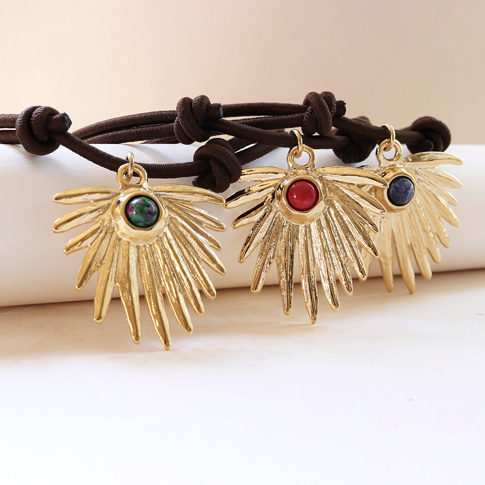 Collares dorados con colgantes en forma de sol y gemas rojas, verdes y azules, sobre cordón marrón.