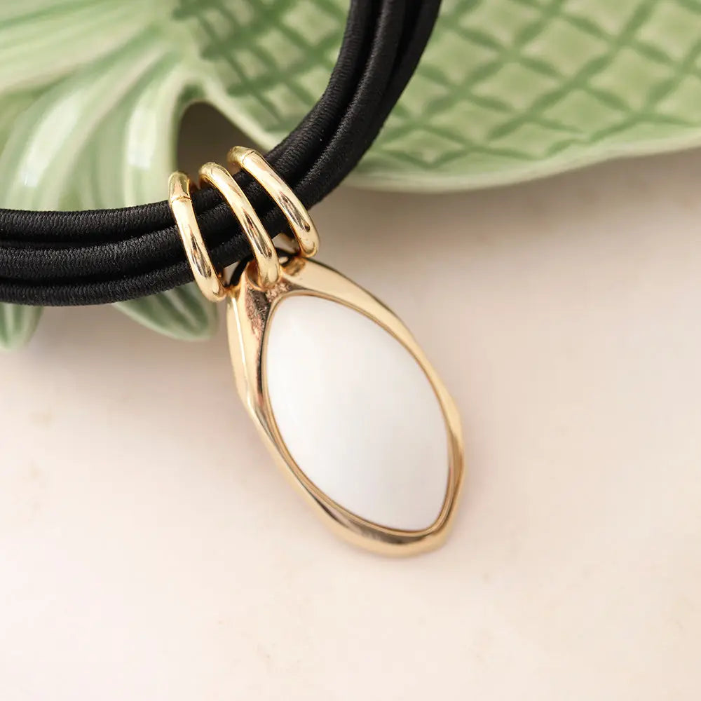 Collar moderno con colgante blanco de cerámica y detalles dorados, sobre cordón negro.
