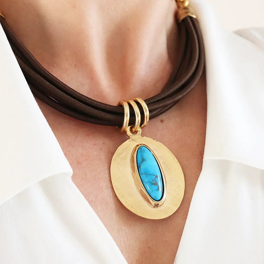 Collar de cuero marrón con medallón dorado y piedra turquesa, estilo moderno y elegante.
