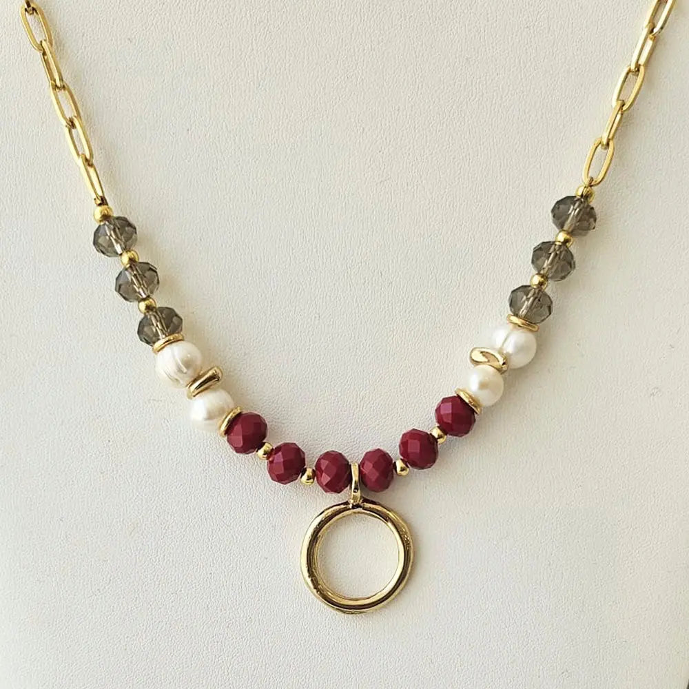 Collar de perlas blancas, cuentas rojas y grises, con eslabones dorados y un colgante circular.