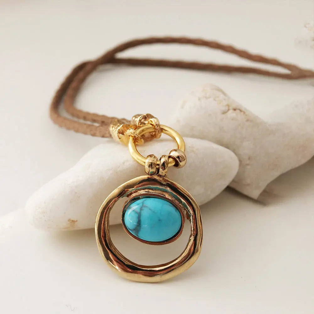 Collar de cuero trenzado con colgante dorado y piedra turquesa en forma ovalada. Elegante y bohemio.