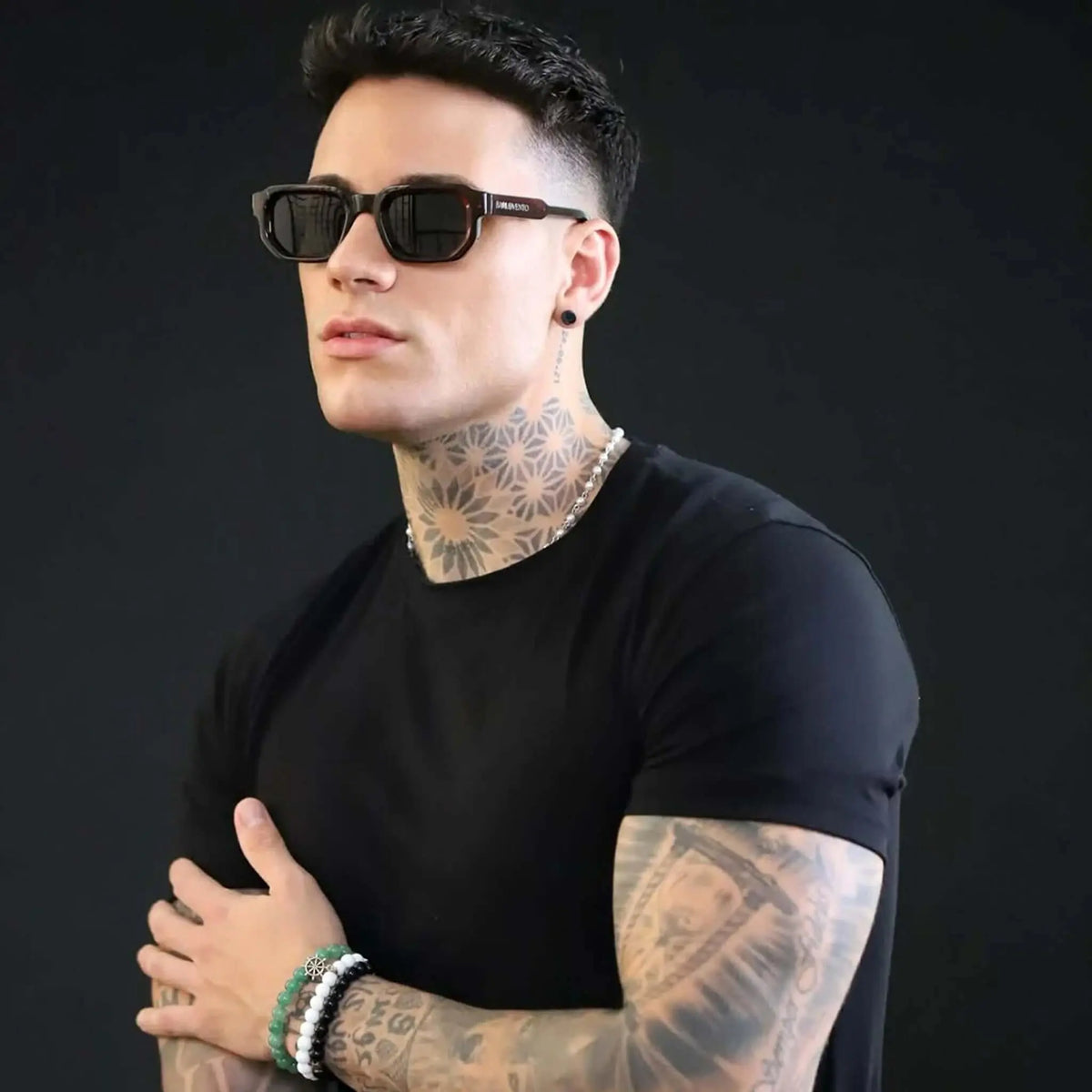 Gafas de sol rectangulares en rojo intenso con lentes verdes oscuros, estilo moderno sobre hombre con tatuajes.
