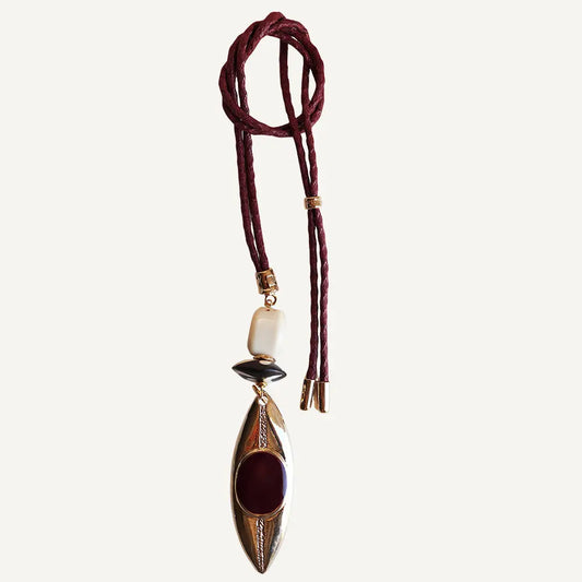 Collar largo de cuero burdeos con colgante ovalado dorado y piedras negras y rojas. Diseño moderno y bohemio.