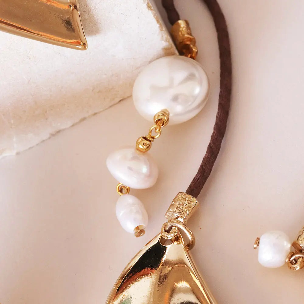 Collar de perlas blancas con detalles dorados y cordón marrón, estilo elegante y moderno.