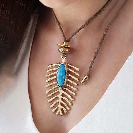 Collar bohemio con colgante dorado en forma de hoja y piedra azul, hecho de metal y cuerda natural.