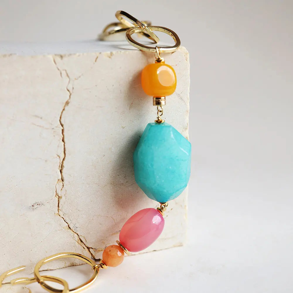 Collar de piedras preciosas en tonos azul, naranja y rosa, con detalles en dorado, estilo bohemio y moderno.