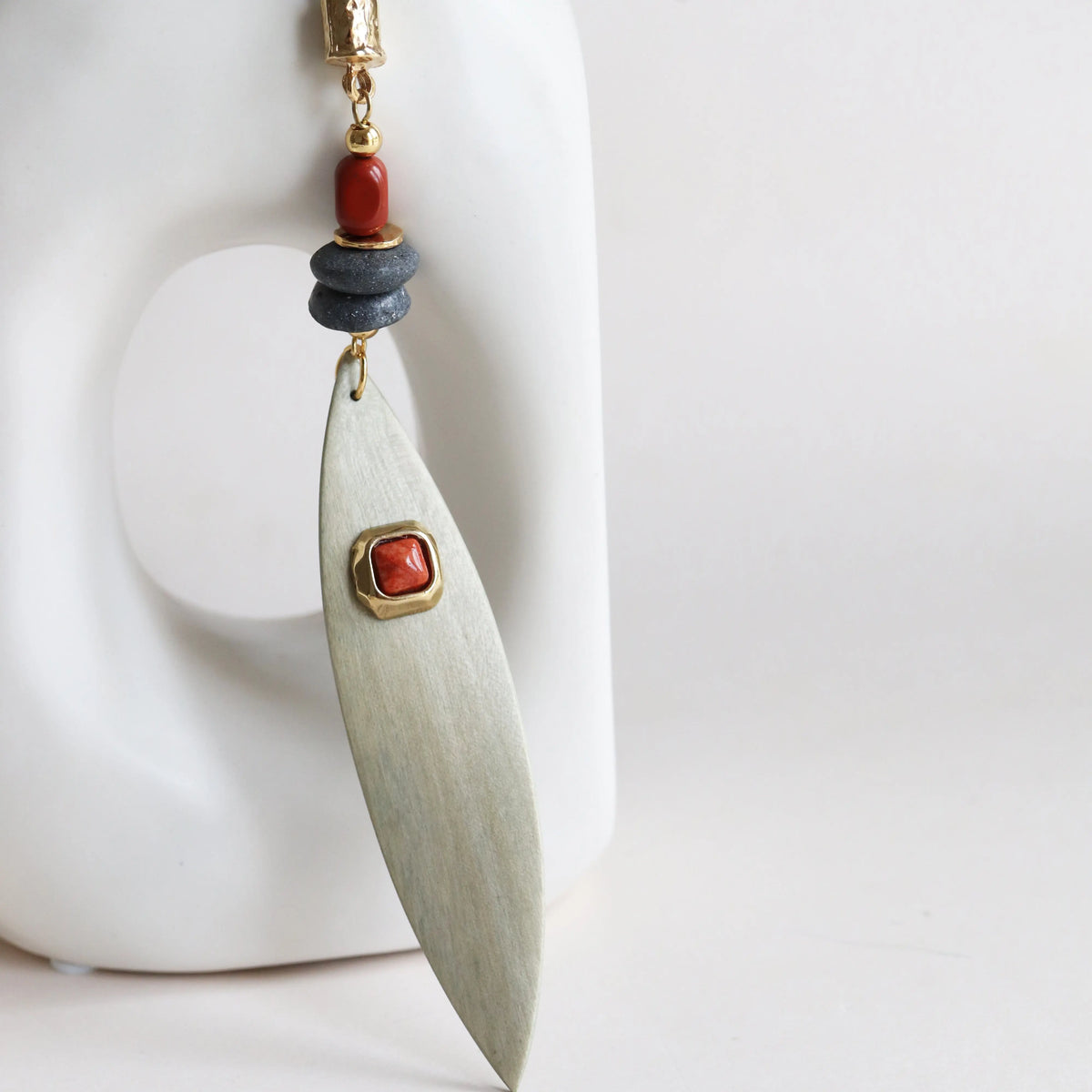 Aretes de metal en forma de hoja con detalles en rojo y gris, estilo moderno y artesanal.