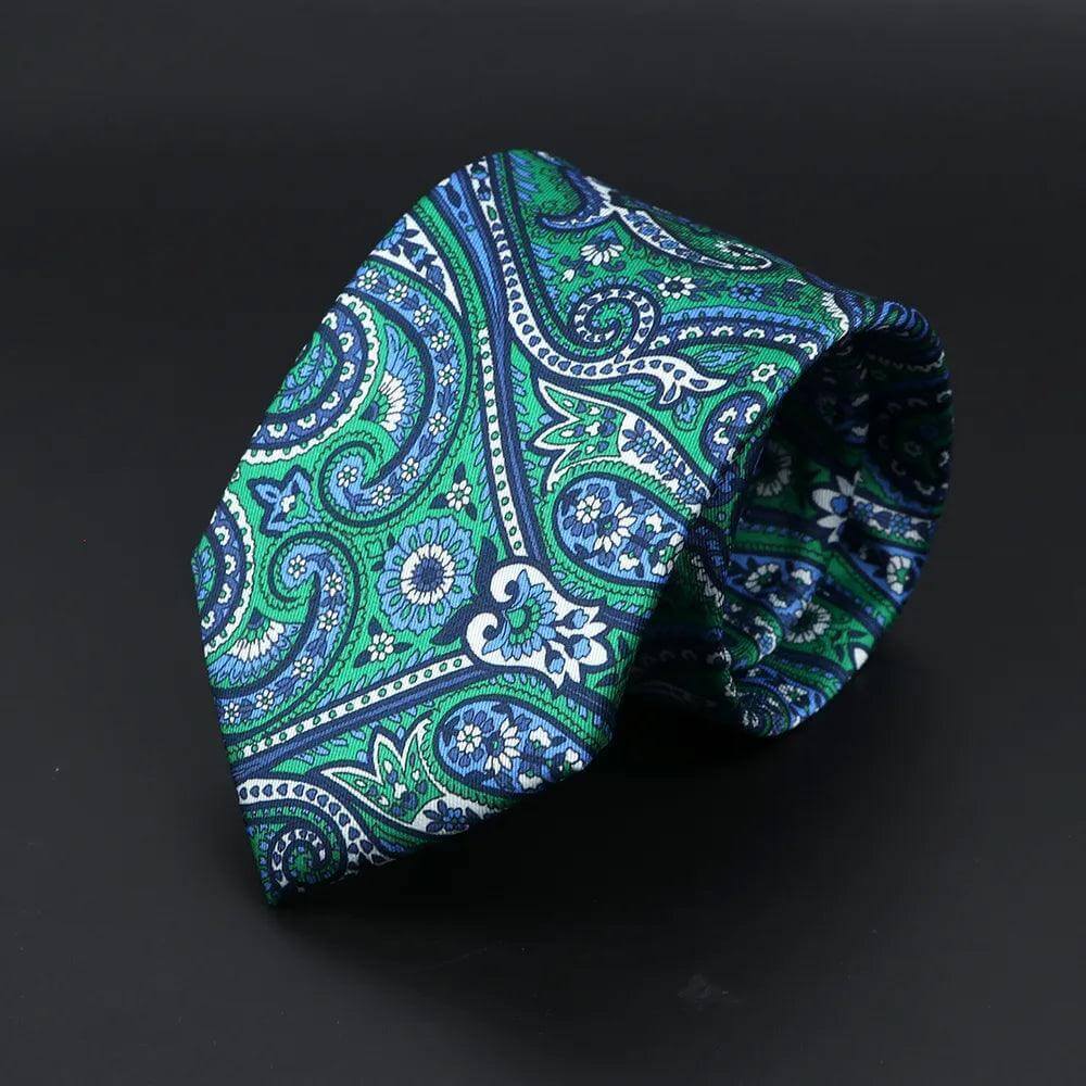 Corbata de seda con elegante estampado paisley en tonos verde y azul sobre fondo oscuro, textura suave y satinada.