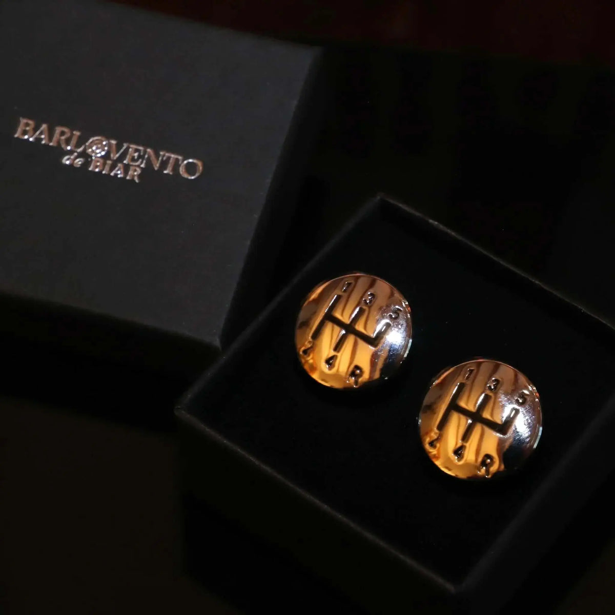 Gemelos redondos de metal dorado con diseño de palanca de cambios manual de 5 velocidades en estuche negro.