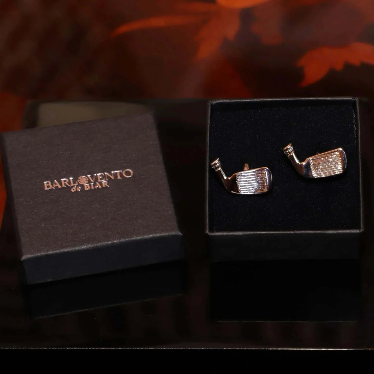 Gemelos para camisa con forma de palos de golf de metal plateado brillante en caja de regalo negra.