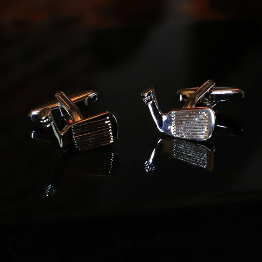 Gemelos plateados con forma de palo de golf. Accesorio elegante con acabado metálico brillante sobre fondo oscuro.