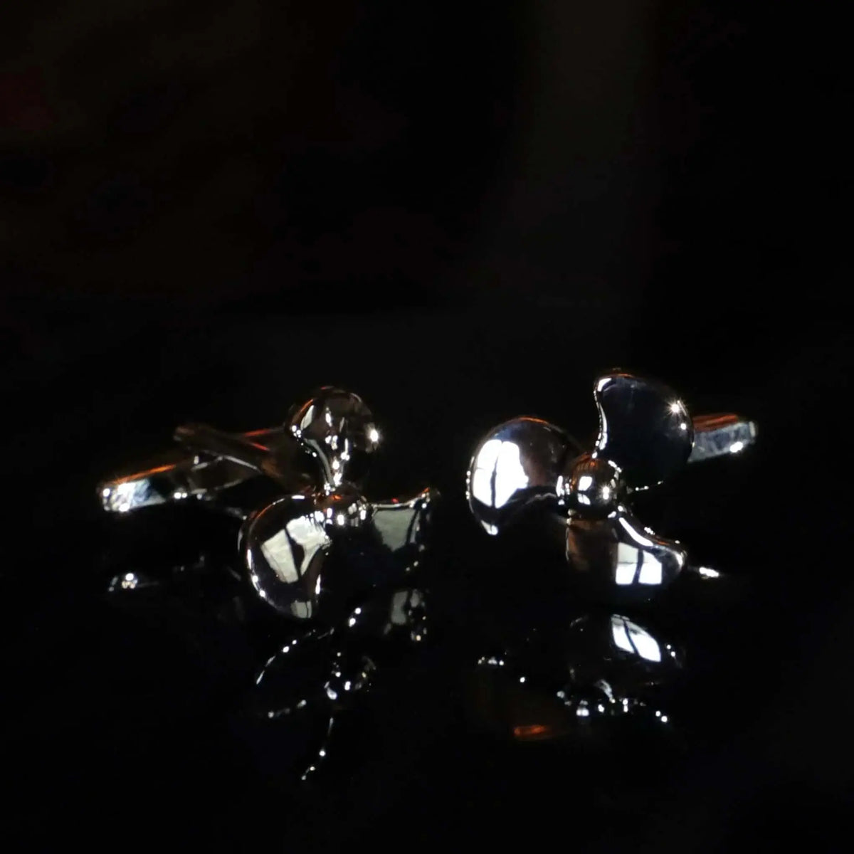 Gemelos de camisa plateados con forma de hélice de barco, acabado metálico brillante sobre fondo negro.