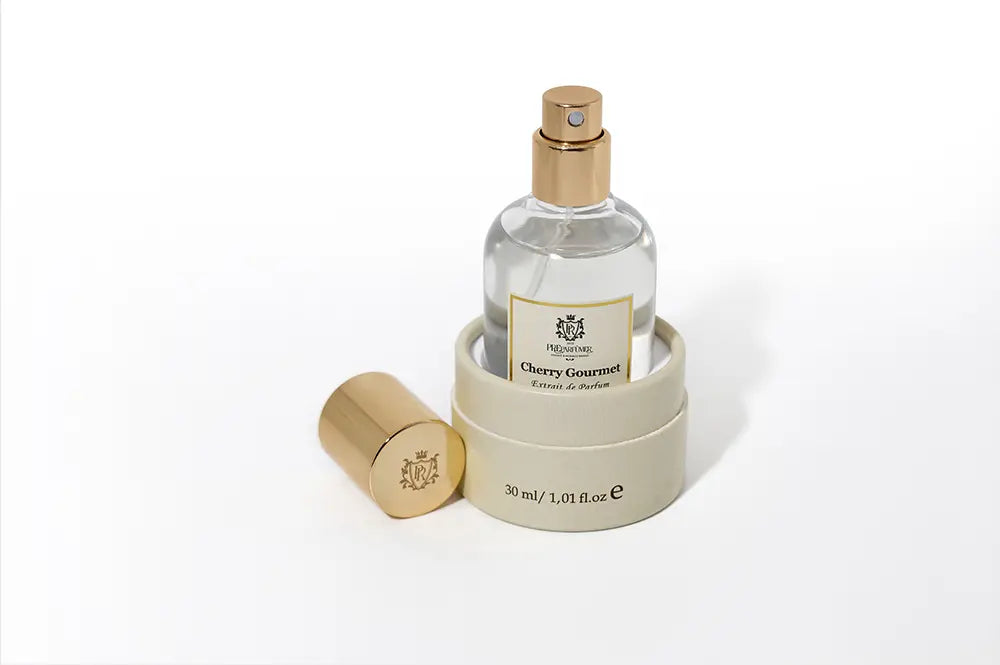 Cherry Gourmet extrait de parfum bottle in a round beige box, with a separate gold cap on a white background.