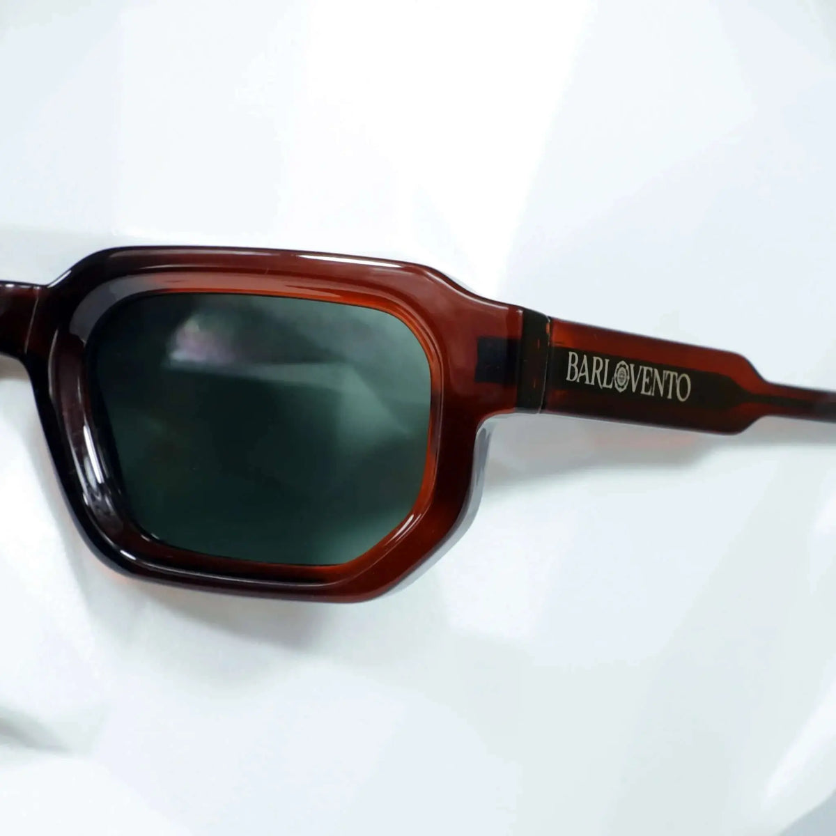 Gafas de sol rectangulares con montura de acetato marrón rojizo y lentes oscuras de tono verdoso.