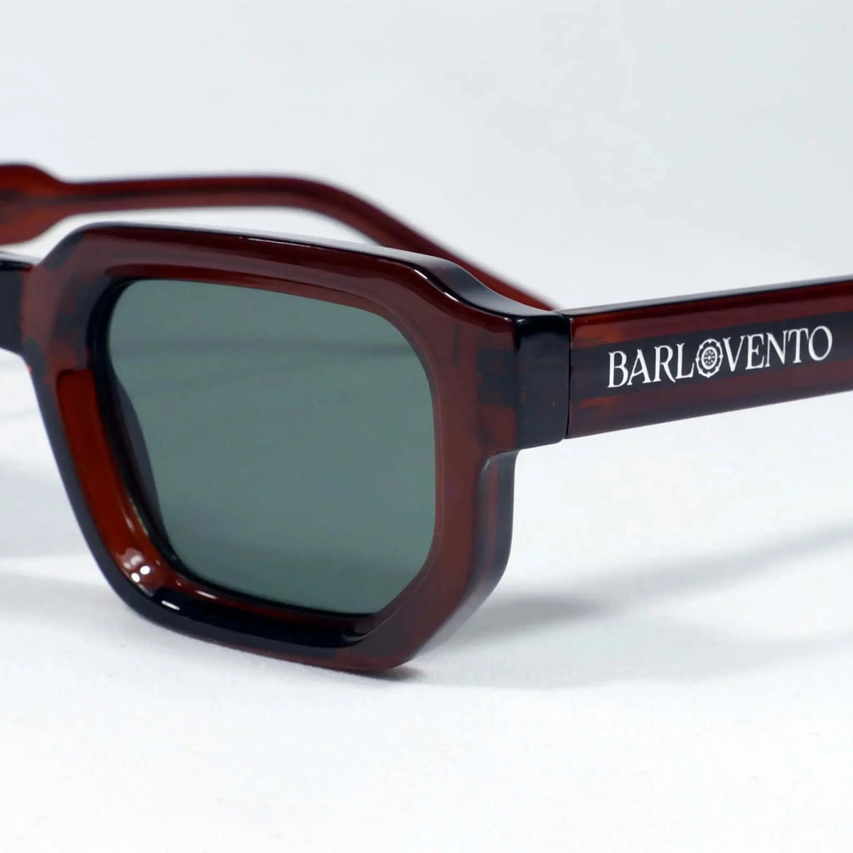 Gafas de sol rectangulares en acetato rojo oscuro traslúcido con lentes verdes oscuras. Estilo moderno y definido.