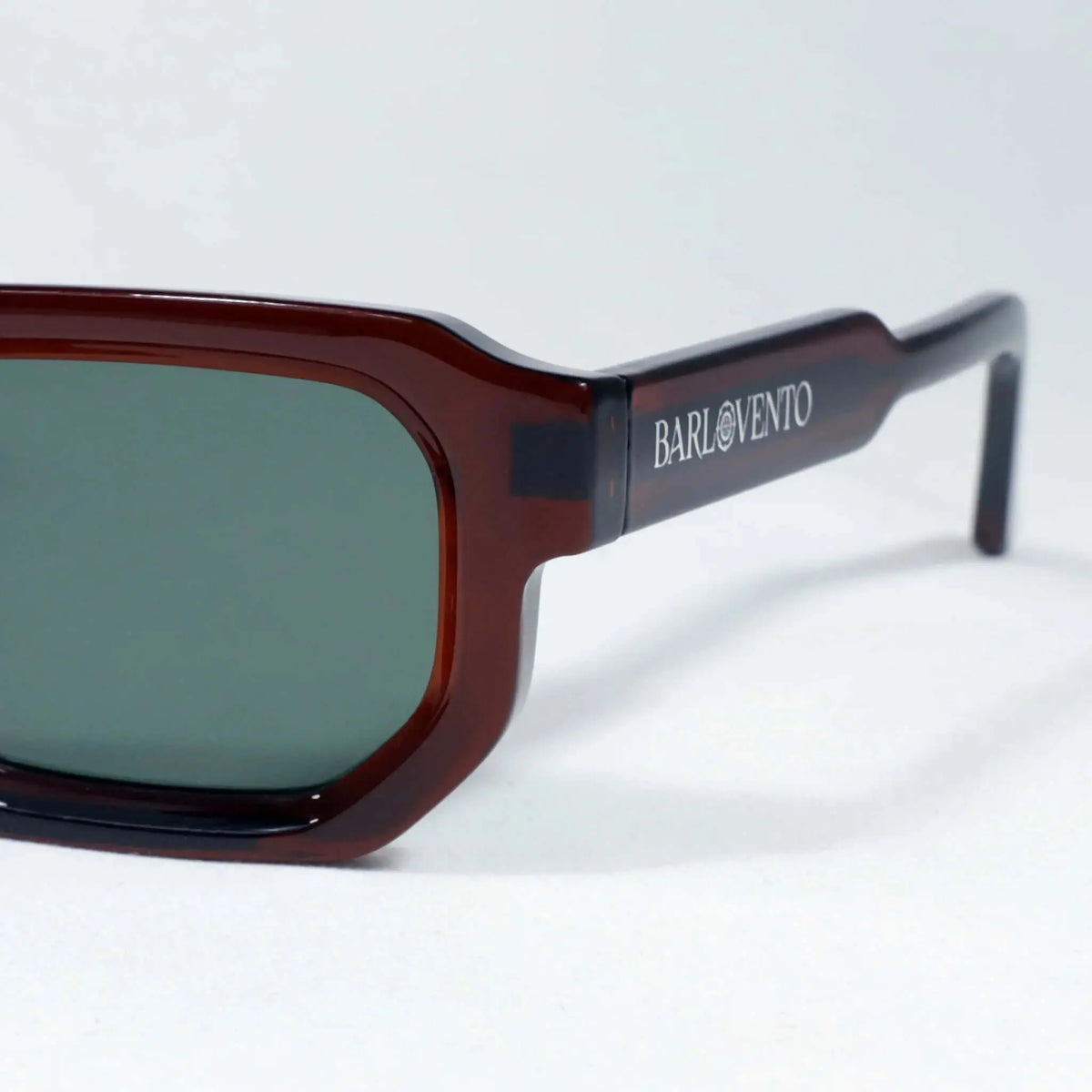 Gafas de sol de montura rectangular color rojo sangre, acabado brillante y lentes verdes sobre fondo blanco.
