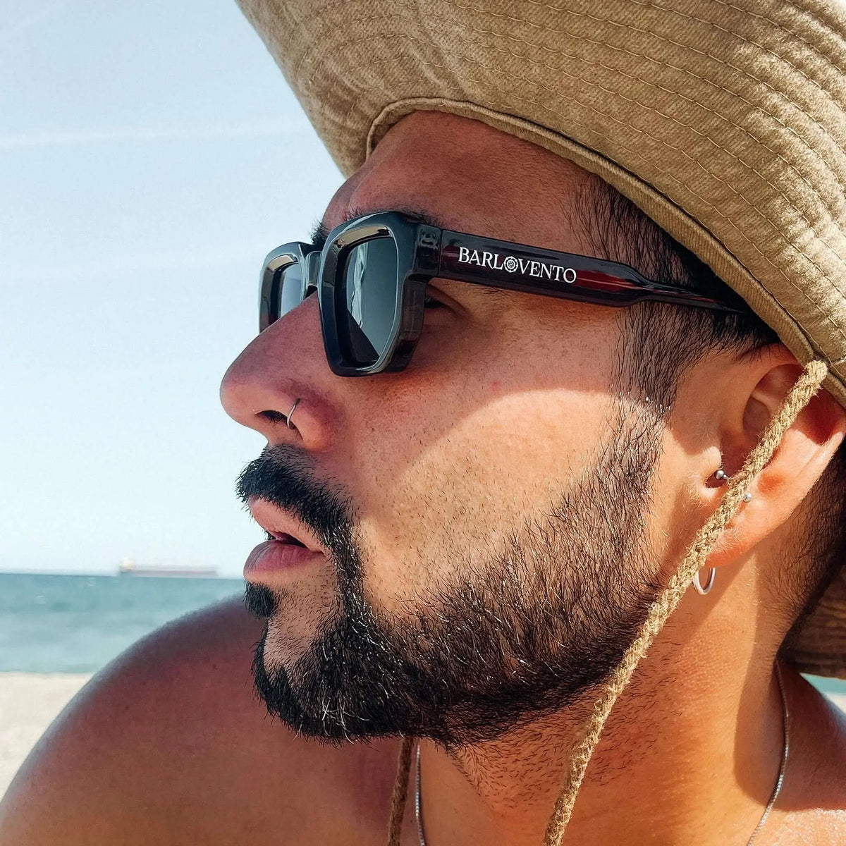 Gafas de sol de montura cuadrada color rojo oscuro y lentes verdes, estilo clásico, usadas por un hombre con sombrero.