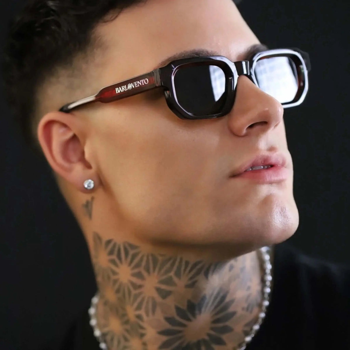 Gafas de sol de diseño geométrico con montura roja degradada y lentes oscuras puestas en un modelo con tatuajes.