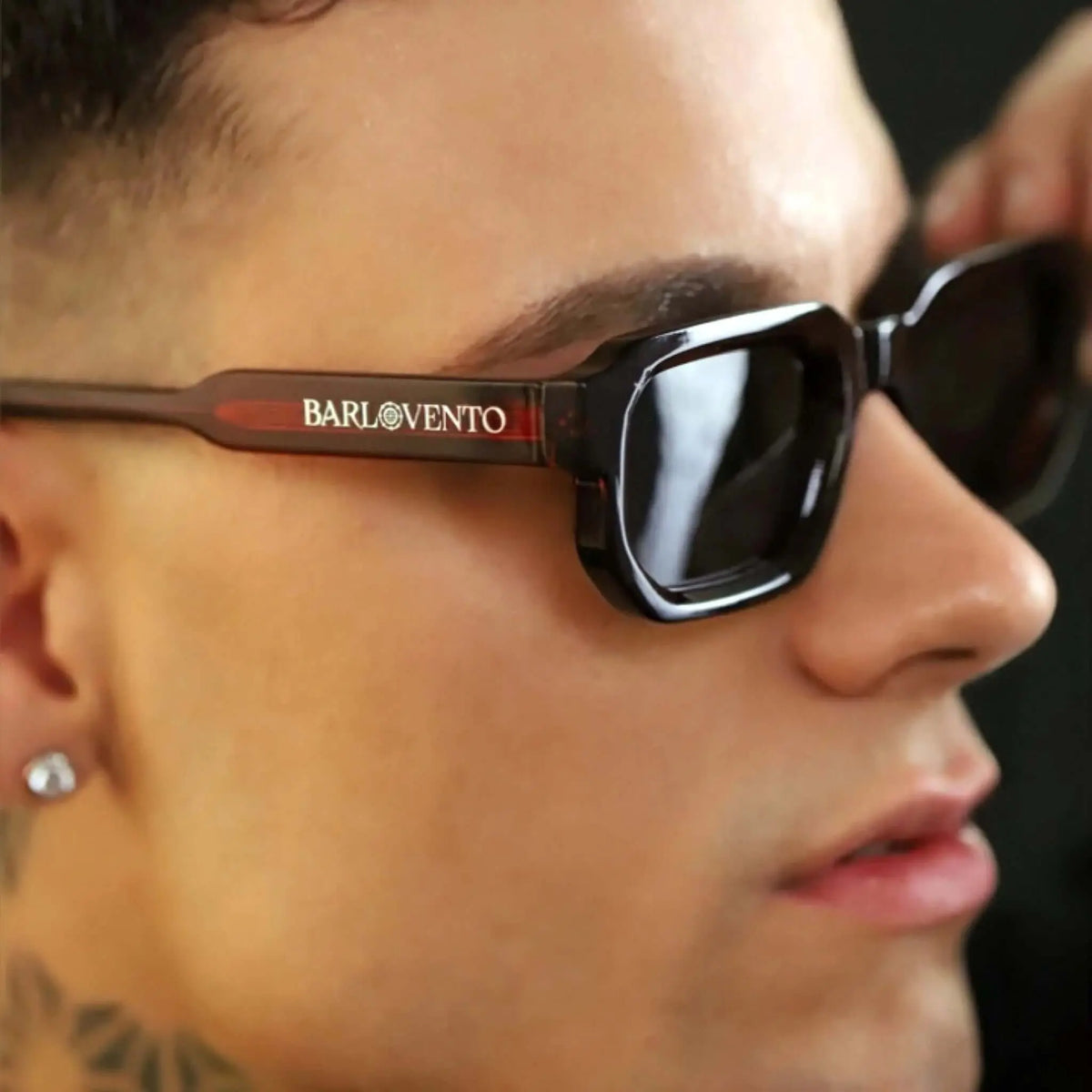 Gafas de sol rectangulares con montura rojo oscuro traslúcido y lentes oscuras, puestas en el rostro de un hombre.