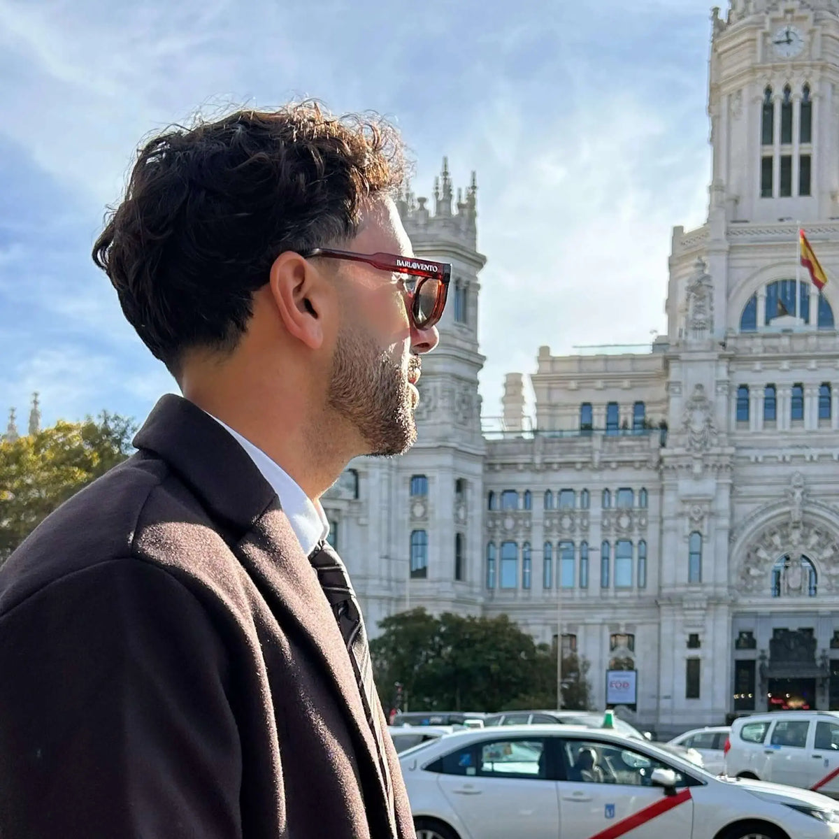 Gafas de sol con montura color rojo traslúcido y lentes oscuras, diseño cuadrado moderno en perfil de hombre.