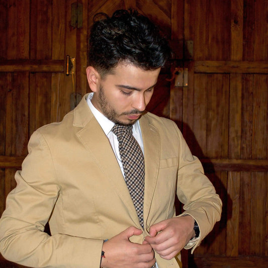 Hombre con americana beige y camisa blanca luciendo una corbata de lana con patrón de pata de gallo en tonos tierra.