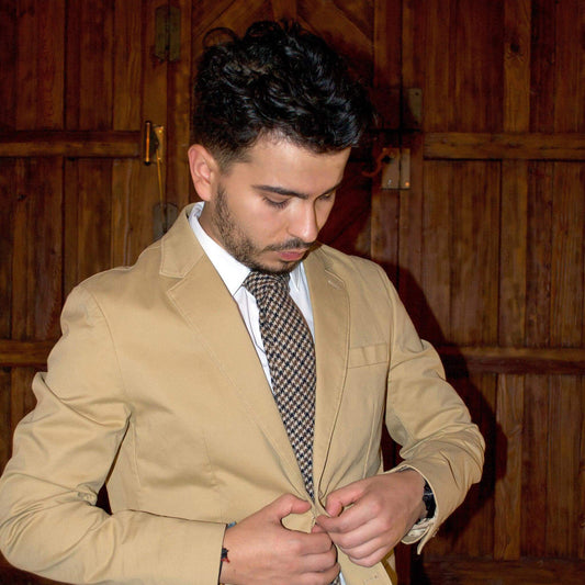 Hombre ajustando su chaqueta mientras lleva una corbata de lana, luciendo elegante frente a un fondo de madera.