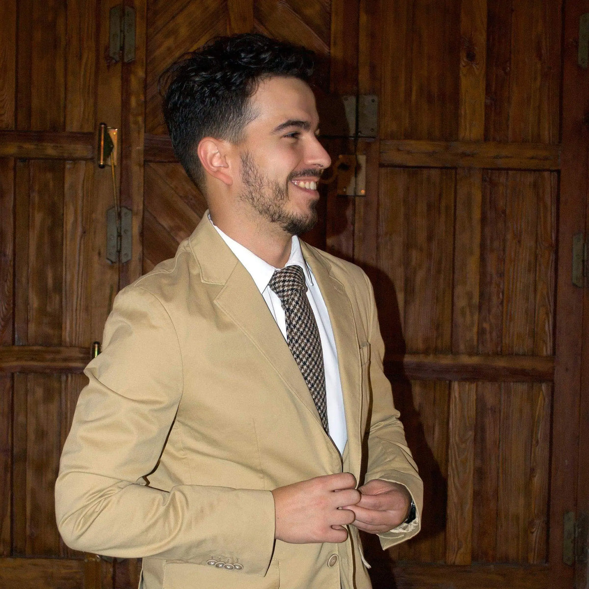 Hombre con chaqueta beige y camisa blanca, luciendo una corbata de lana con patrón de pata de gallo en tonos marrones.