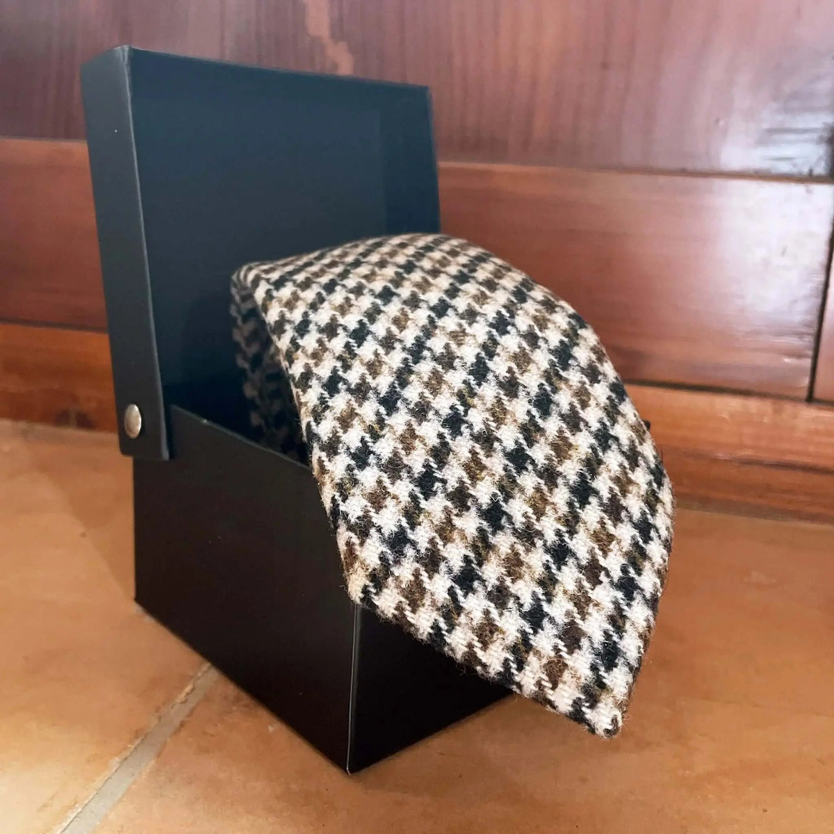 Corbata de lana con patrón de pata de gallo en tonos marrón, negro y crema, presentada en una caja negra.